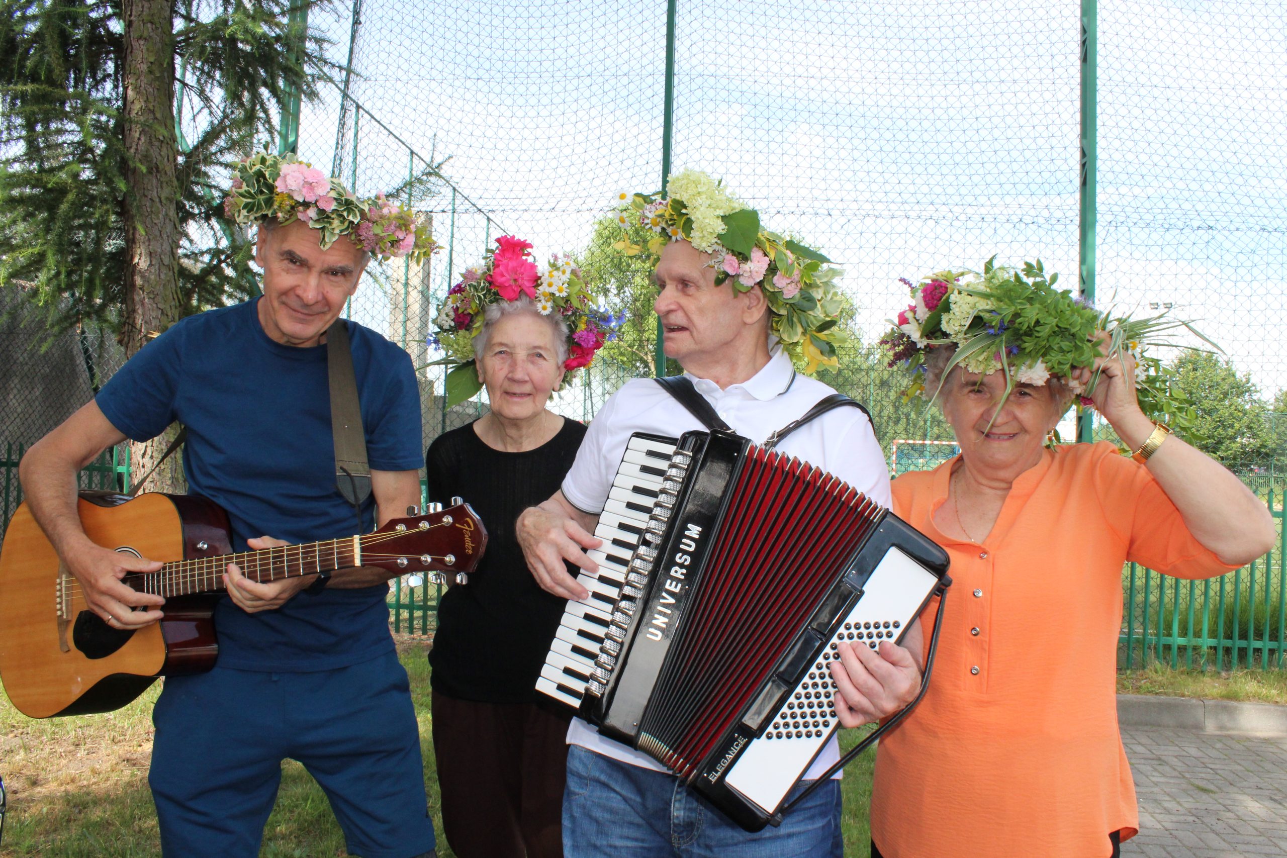6) Na zdjęciu od lewej: mężczyzna z gitarą, seniorka, mężczyzna z akordeonem i seniorka. Wszyscy we wiankach na głowie.