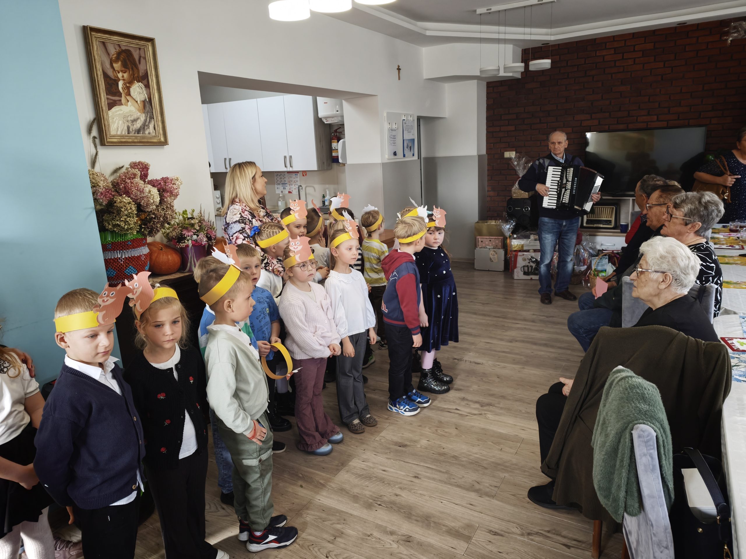 4. Na fotografii widzimy grupę dzieci z przedszkola „Zielony Zakątek” które śpiewają piosenki wraz z seniorem z DDP – Panem Zygmuntem, który przygrywa na akordeonie