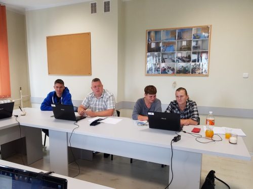 Na zdjęciu znajdują się cztery osoby siedzące przy stole. Przed nimi stoją laptopy.