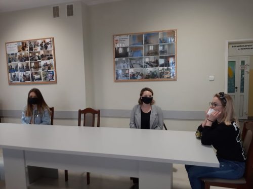 Na zdjęciu znajdują się trzy osoby siedzące przy stole. Wszyscy mają na twarzy maseczki.