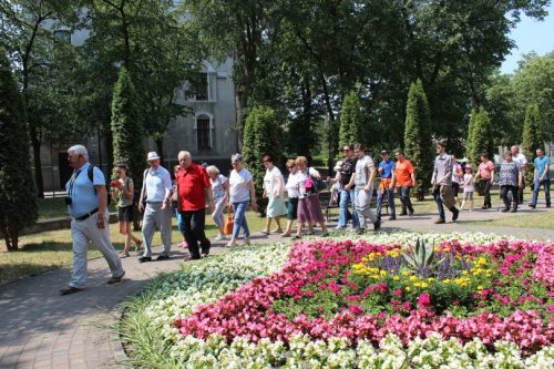 Na zdjęciu przewodnik prowadzący wycieczkę. Z prawej strony kolorowy dywan kwiatowy.