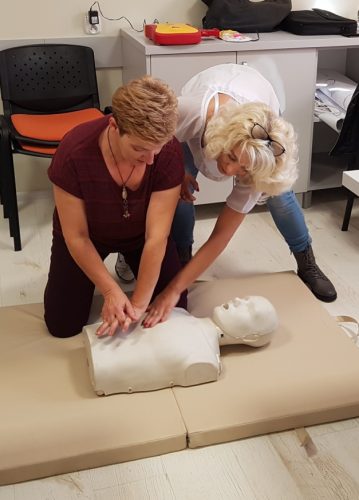 Na zdjęciu znajdują się dwie kobiety. Na podłodze leży tułów manekina. Jedna z kobiet uczy drugą techniki masażu serca.